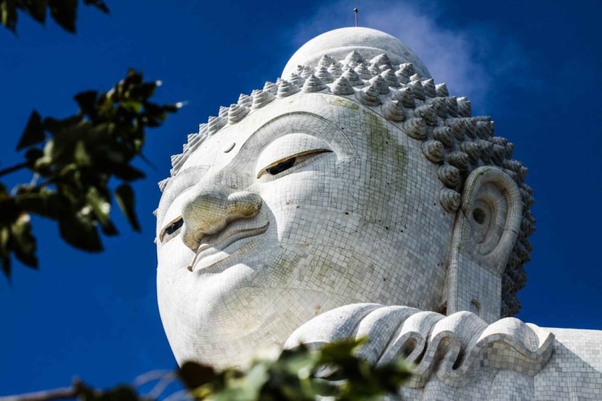 A large, white, stone Buddha statue with intricate carvings and a pointed top against a clear blue sky. 4