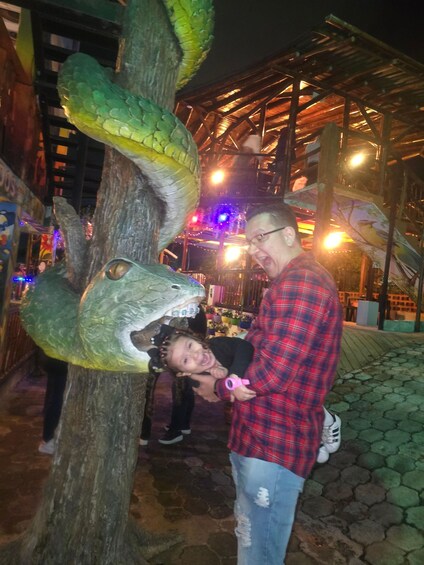 A person in a red plaid shirt and jeans standing next to a tree with a large snake sculpture. 4
