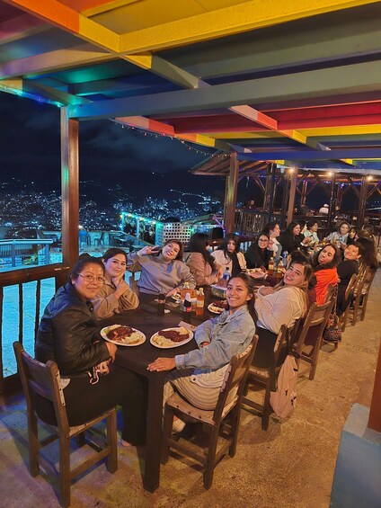 A group of people dining at an outdoor restaurant with a city view at night. 3