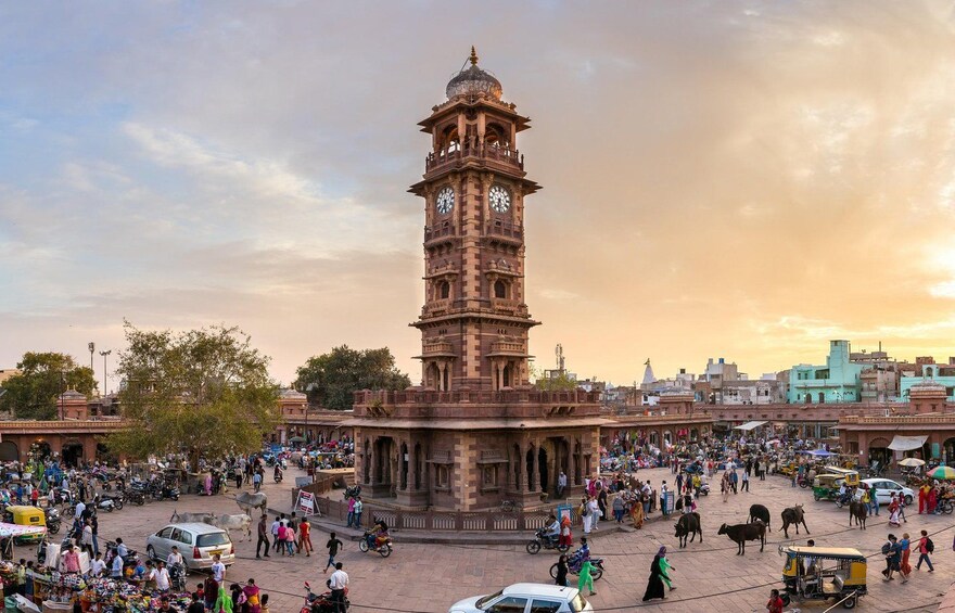 A historic clock tower surrounded by a bustling market area with people and vehicles. 3