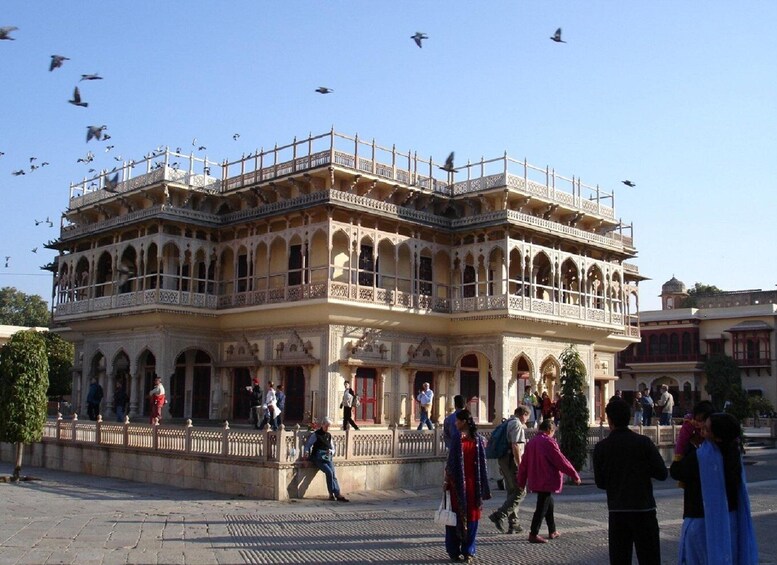 A historic building with ornate architecture and a balcony, surrounded by people and birds. 3