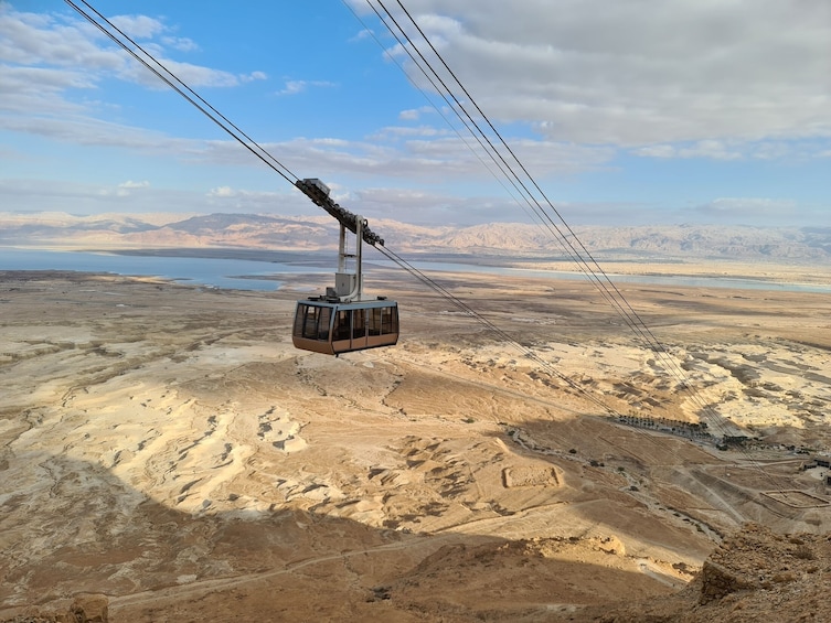 A cable car suspended over a desert landscape with mountains in the background. 4