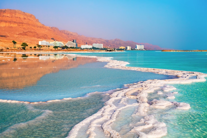 A salt flat with clear water and white salt formations, a desert landscape, and buildings in the background. 3