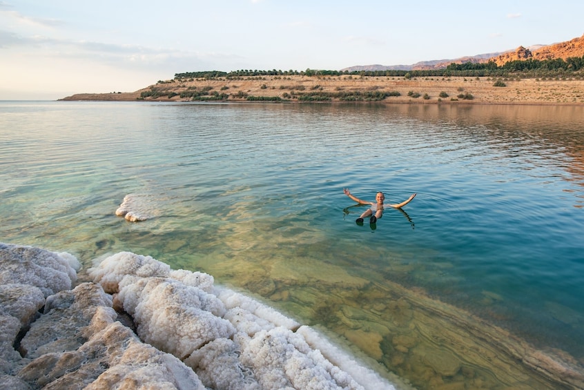 A person swimming in a clear body of water with white mineral deposits at the shore. 2