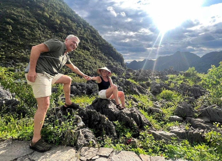 Two people sitting on rocks in a mountainous area with greenery and a cloudy sky. 4