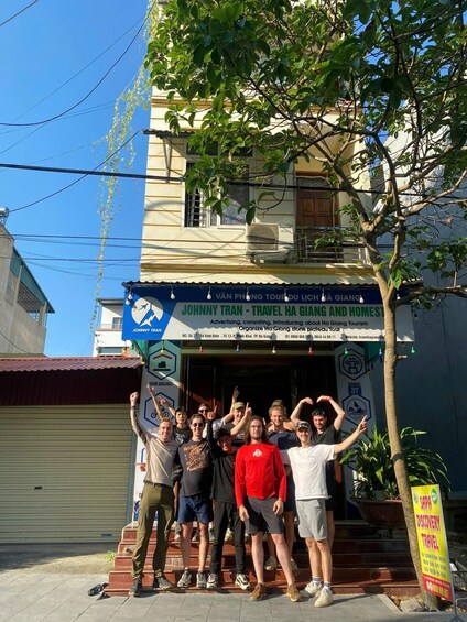 A group of people posing in front of a building with a sign advertising travel services. 3