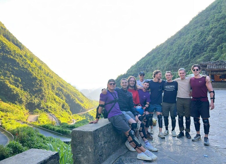 A group of people in outdoor gear posing on a stone ledge with a mountainous landscape in the background. 2