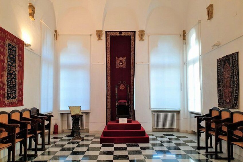 Una habitación con piso a cuadros, alfombra roja y una silla roja en el centro. 3