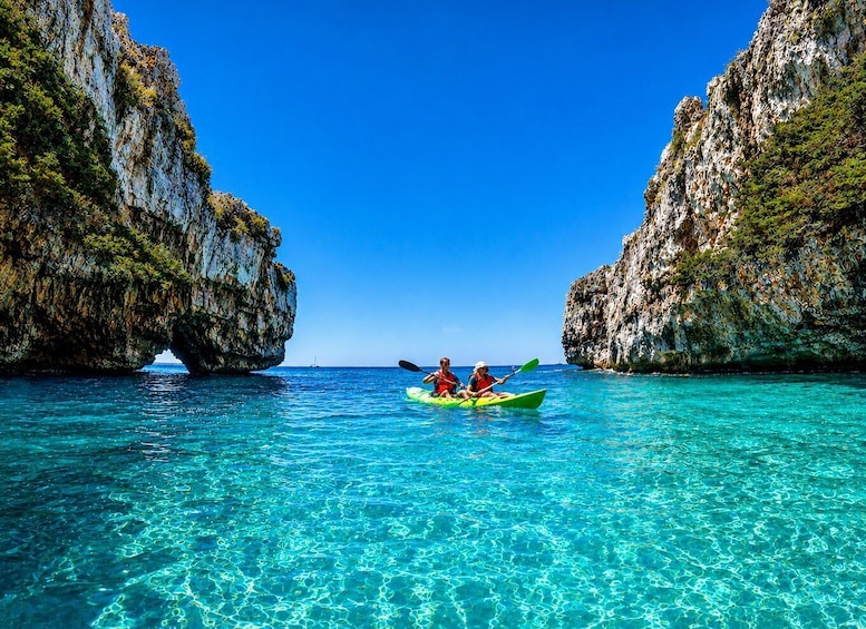 Two people kayaking in clear turquoise waters between rocky cliffs. 1