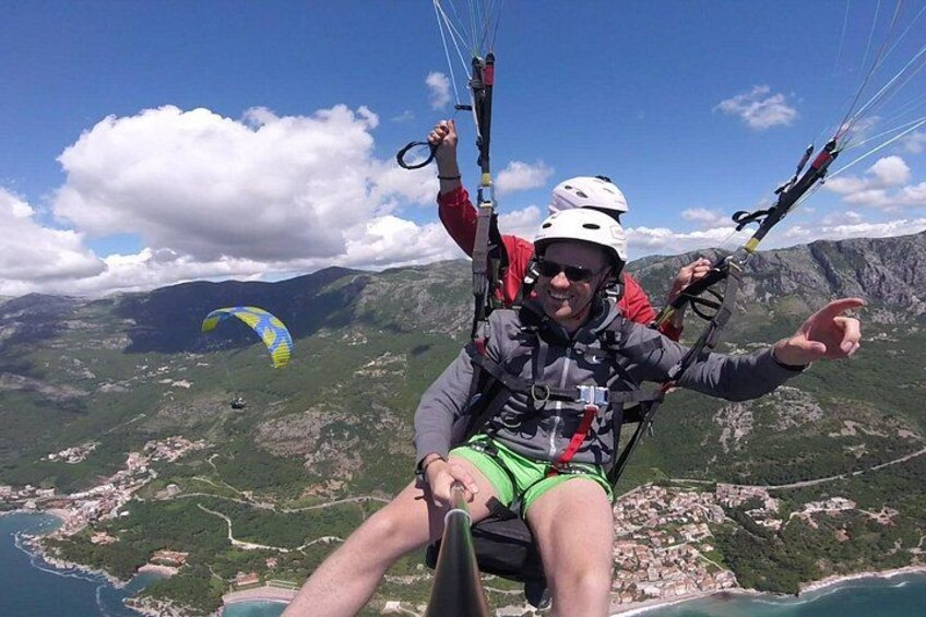 Una persona practicando parapente con montañas y la costa al fondo. 1