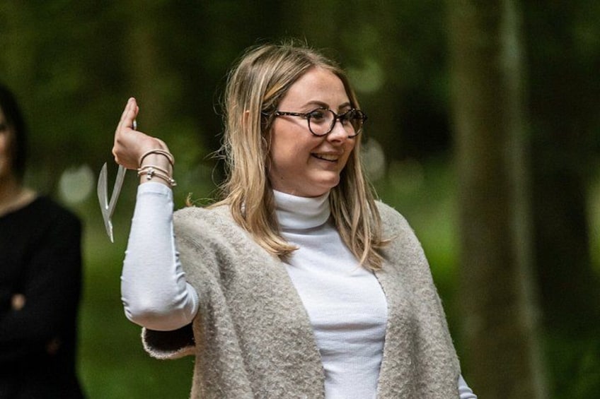 A person in a white turtleneck and grey cardigan, holding a pair of scissors. 3