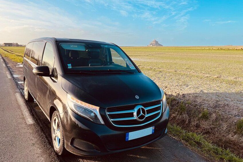 Un furgone nero Mercedes parcheggiato su una strada, con cielo sereno e una collina in lontananza. 3