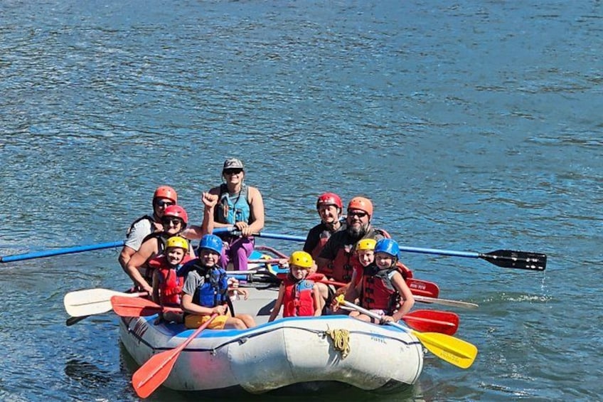 A group of people on a white inflatable raft with paddles, floating on calm water. 3