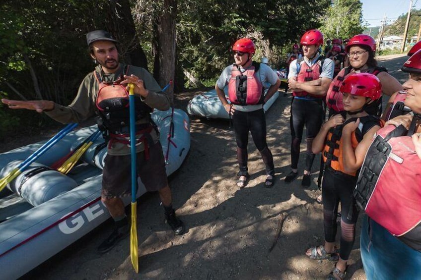 Un groupe de personnes portant des casques et des gilets de sauvetage, se tenant près de kayaks et d’une planche à pagaie. 2