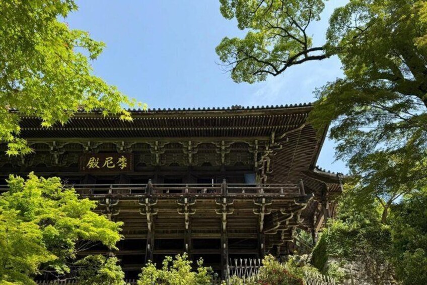 Ein traditionelles japanisches Gebäude mit einem Ziegeldach und Holzkonstruktion, umgeben von üppigem Grün. 5