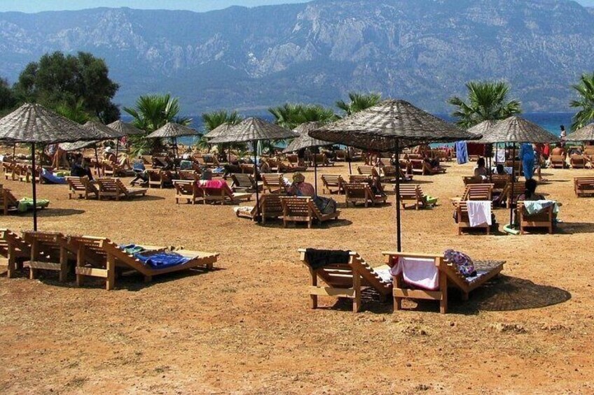 A beach with wooden lounge chairs and thatched umbrellas, palm trees, and mountains in the background. 2