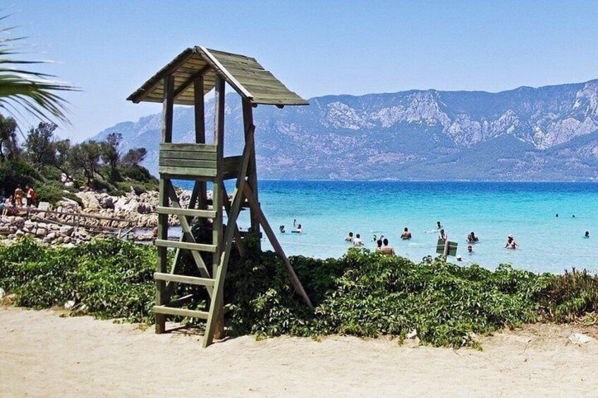 A wooden lifeguard tower on a beach with clear blue water and mountains in the background. 5