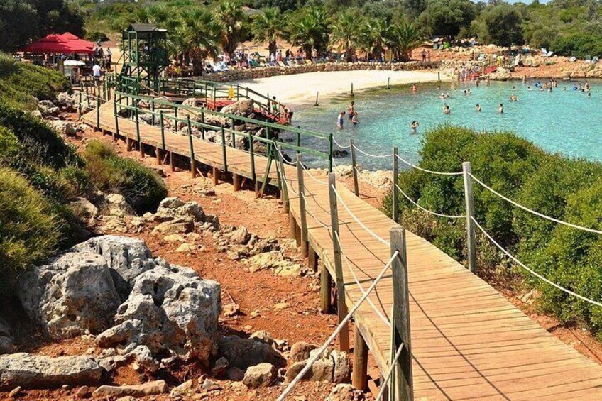 A beach with a wooden boardwalk, clear blue water, and people swimming. 3