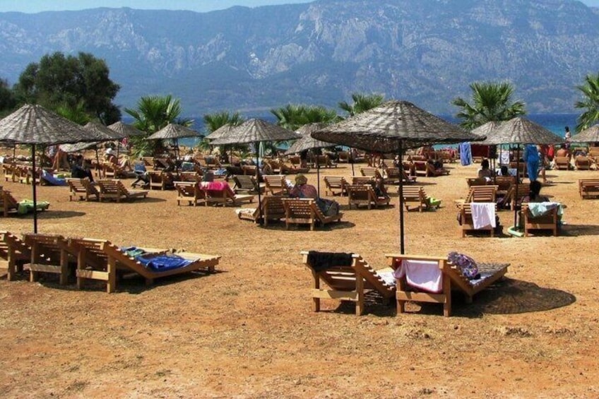 A beach with wooden lounge chairs and thatched umbrellas, palm trees, and mountains in the background. 2
