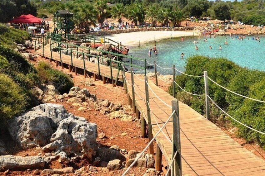 A beach with a wooden walkway, people swimming, and palm trees. 4
