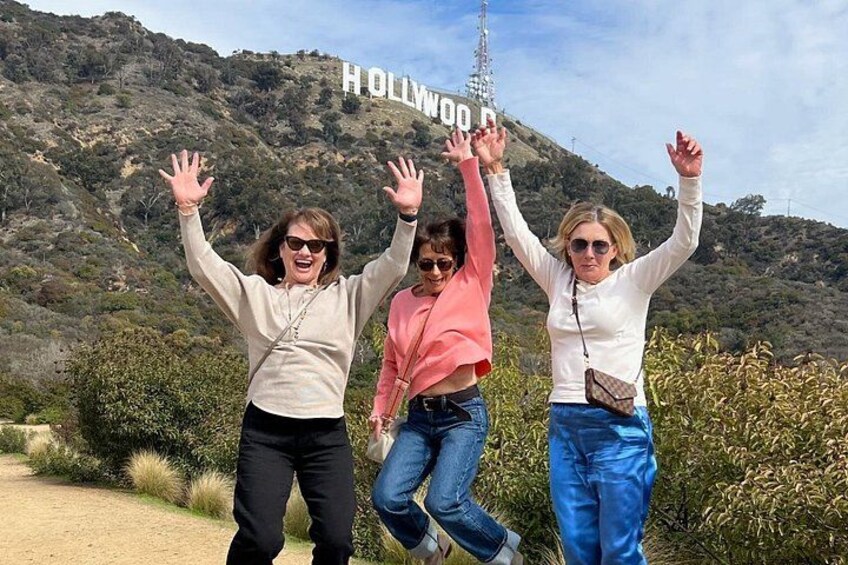Three people standing in front of the Hollywood sign with their arms raised. 4