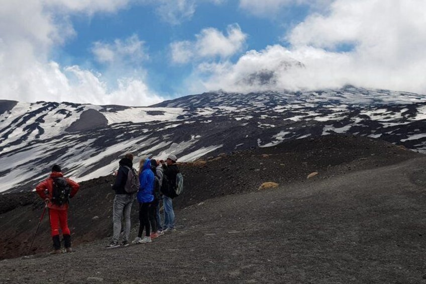 A group of hikers on a volcanic terrain with snow patches and a clear sky. 4