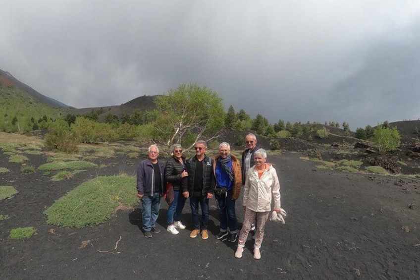 A group of people standing on a volcanic landscape with green vegetation and hills in the background. 3