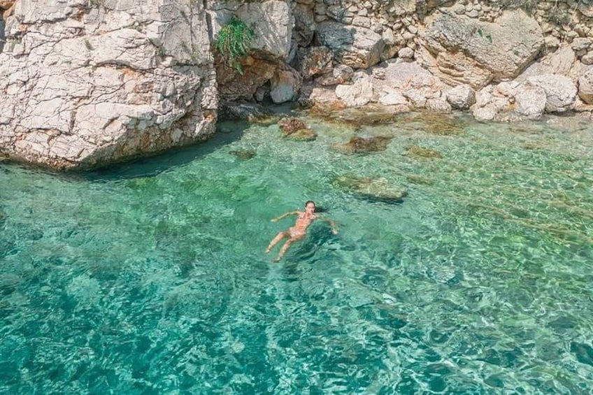 A person swimming in clear water near rocky cliffs. 4