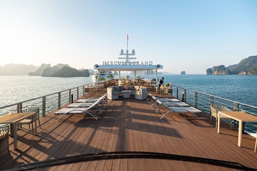 A wooden deck with lounge chairs and a covered seating area on a boat named 'Hercules Grand'. 2
