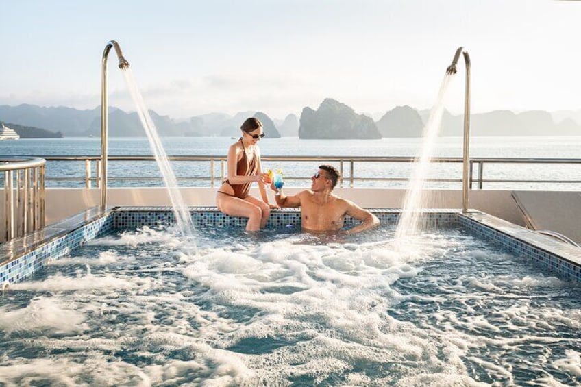 A couple in a hot tub with water jets, overlooking a body of water and distant islands. 5