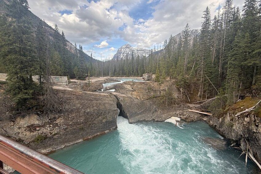 Une rivière qui traverse un canyon boisé, avec des affleurements rocheux et un pont au premier plan. 4