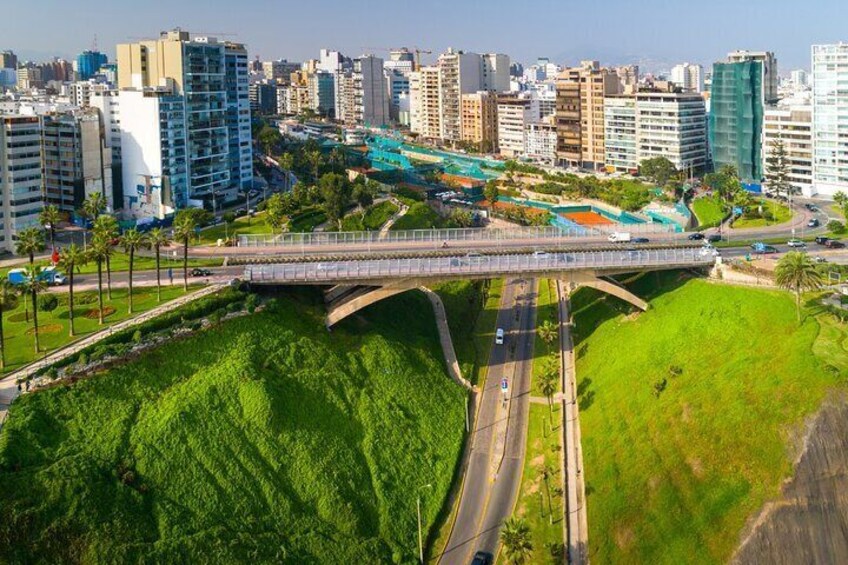 A bridge over a green park with city buildings in the background. 3