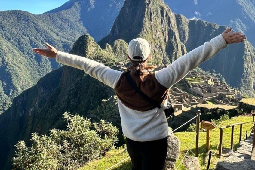 A person standing with arms outstretched, overlooking a mountainous landscape with a village below. 5