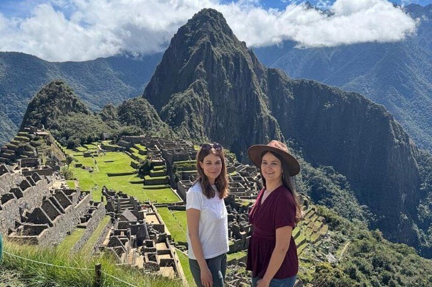 Two people standing in front of Machu Picchu ruins with a mountain in the background. 2