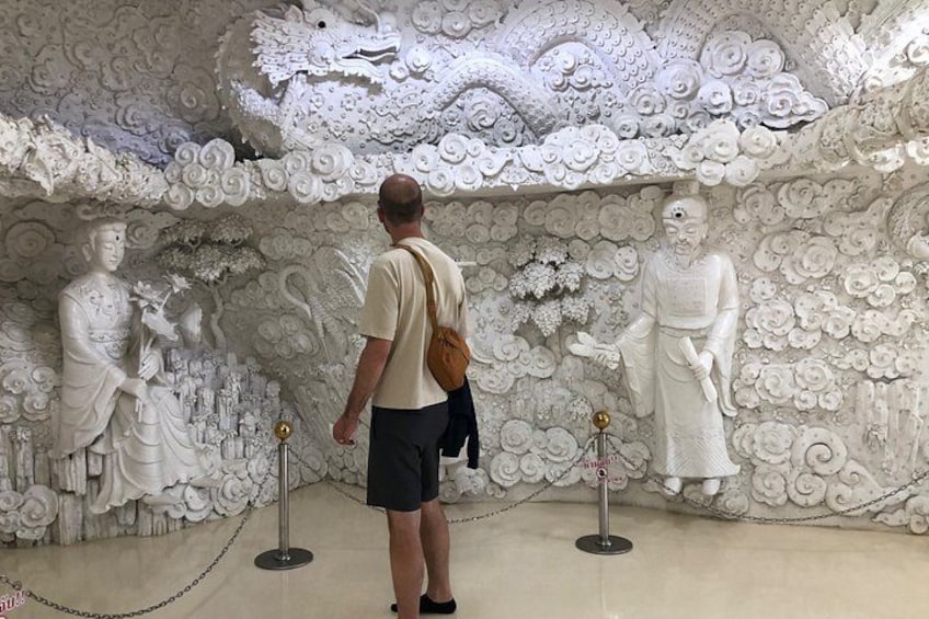Un hombre de pie frente a una pared con delicados relieves blancos y estatuas. 4
