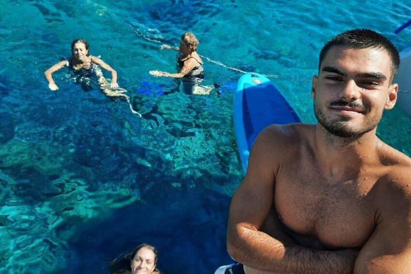A clear blue sea with people swimming and a surfboard. 2