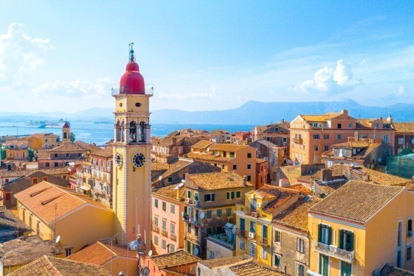 Une ville côtière qui se distingue par son imposant clocher, ses bâtiments aux toits de tuiles rouges et sa vue dégagée sur la mer et les montagnes en arrière-plan. 1