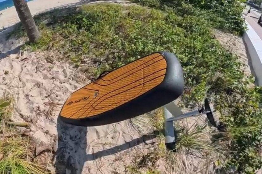 Un banc en bois avec une assise et un dossier noirs, situé sur une plage de sable bordée de végétation. 5