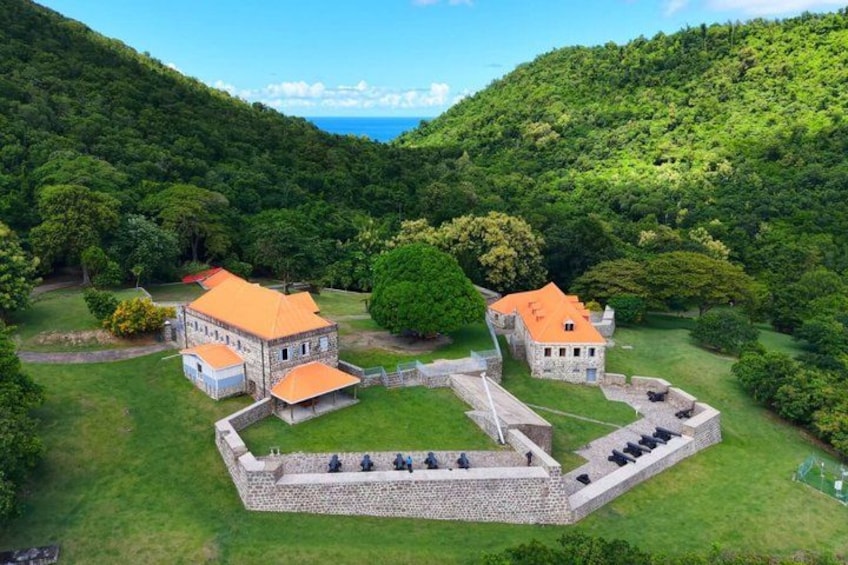 A historic fort with two buildings, surrounded by lush greenery and a mountainous backdrop. 4