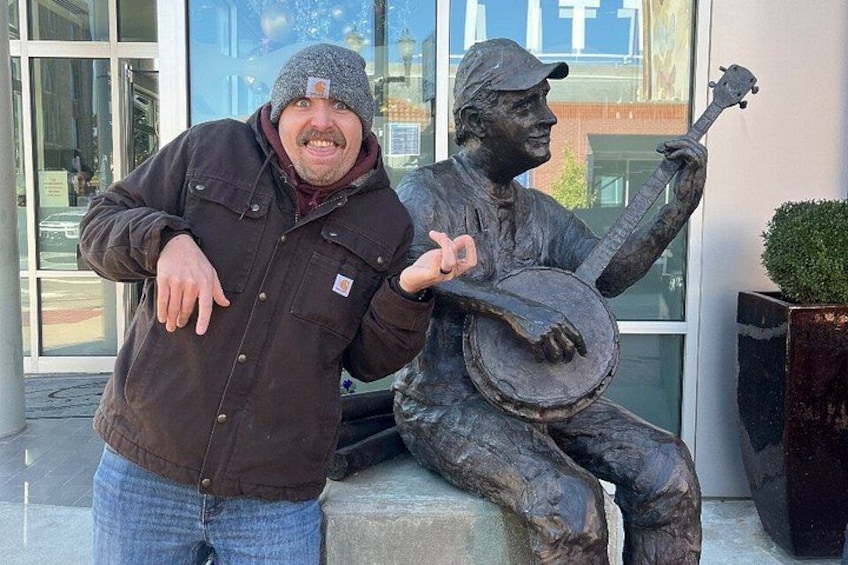 A person standing next to a statue of a man playing a banjo. 1