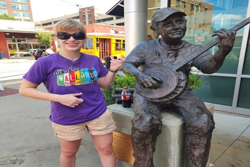 A person standing next to a bronze statue of a man playing a banjo. 4