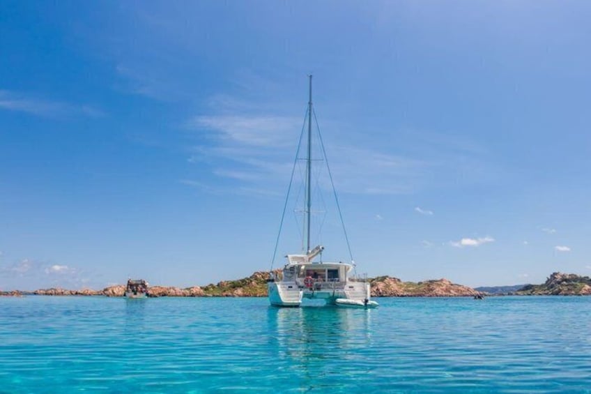 A white sailboat on calm turquoise waters with rocky terrain in the background. 4