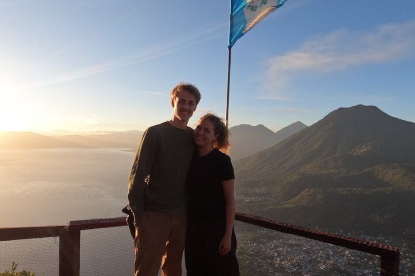 A couple standing on a wooden railing with a mountainous landscape in the background. 4