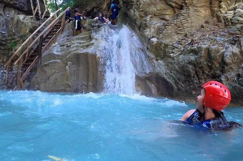 Une personne vêtue d’un maillot de bain bleu et d’un casque rouge, sur un toboggan aquatique avec une cascade. 1