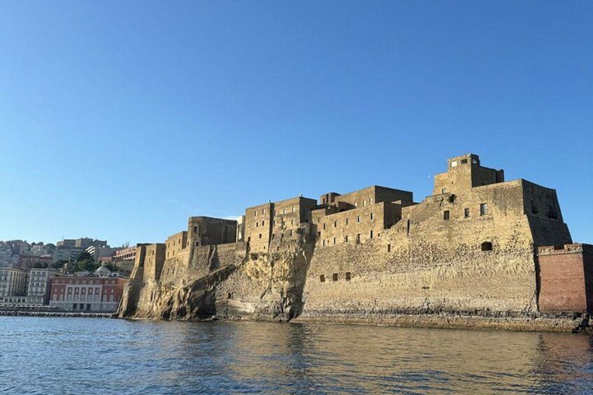 A historic stone fortress by a body of water, with a clear sky above. 1