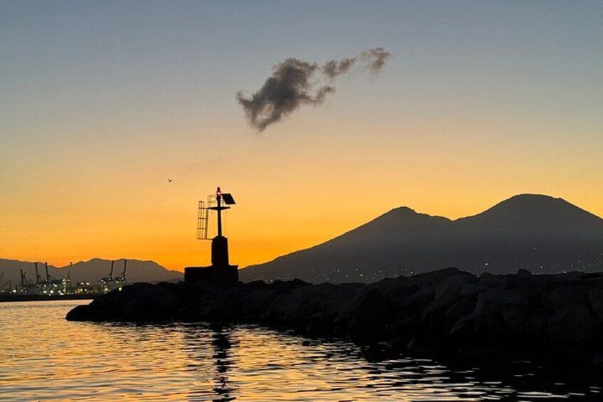 A sunset over a body of water with a lighthouse and mountains in the background. 4