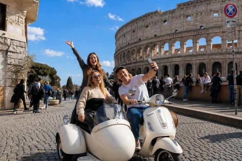 A couple on a vintage Vespa scooter in front of the Colosseum with tourists in the background. 4