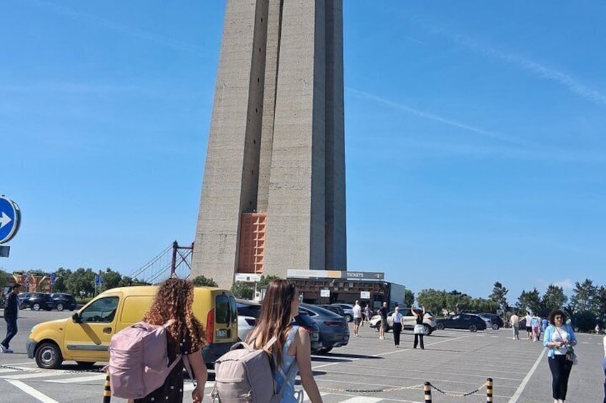 Un monumento alto, una camioneta amarilla y personas caminando en un estacionamiento. 2