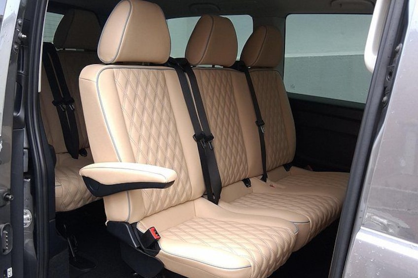 Interior de coche con asientos color crema acolchados, cinturones de seguridad negros y un picaporte visible. 5