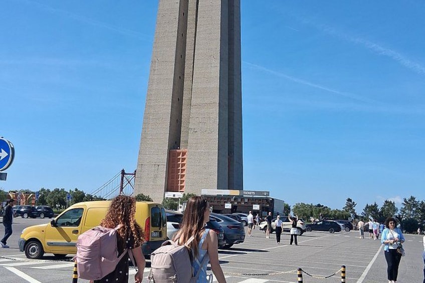 Un monumento alto, una furgoneta amarilla y personas caminando en un estacionamiento. 2